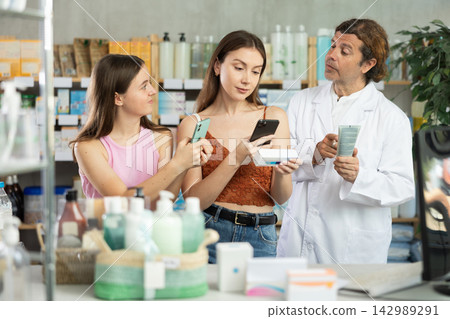 Mom and teen girl in pharmacy scans QR code ointment, pharmacist in background offer help 142989291