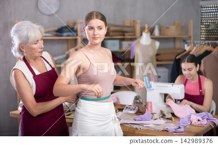 elderly dressmaker takes measurements from a woman in front of an experienced seamstress elderly dressmaker takes measurements from a woman in front of an experienced seamstress 142989376