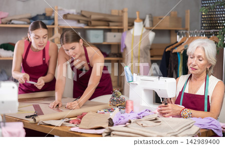 Elderly seamstress working alongside fashion designers in an atelier Elderly seamstress working alongside fashion designers in an atelier 142989400