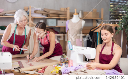 Young tailor sewing, senior and adult employee assistant drawing paper dress pattern by curves Young tailor sewing, senior and adult employee assistant drawing paper dress pattern by curves 142989401
