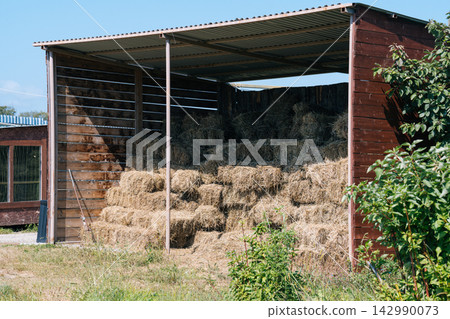 Dry straw hay bales stacked inside wooden shed shelter on farm backyard paddock in autumn harvest season outdoor Dry straw hay bales stacked inside wooden shed shelter on farm backyard paddock in autumn harvest season outdoor 142990073