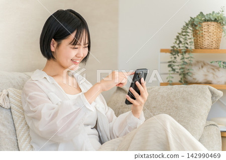 A smiling high school girl is using her smartphone on the sofa at home. A glimpse into the daily life of a teenager enjoying social media. 142990469