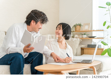 A high school girl discusses her future with her dad at home. Father and daughter think about career paths and college entrance exams together. A high school girl discusses her future with her dad at home. Father and daughter think about career paths and college entrance exams together. 142990704