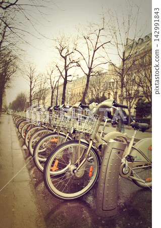 Row Of City Rental Bicycles Lined Up Along Wet Urban Street On Overcast Day Row Of City Rental Bicycles Lined Up Along Wet Urban Street On Overcast Day 142991843
