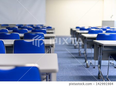A conference room with neatly arranged blue chairs and white desks. A conference room with neatly arranged blue chairs and white desks. 142991984