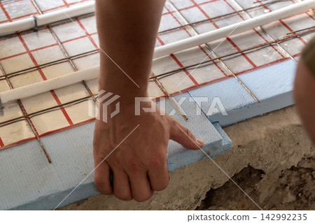 Worker hands mounting underfloor heating pipes on foam board insulation before concrete pour. Modern home improvement, plumbing expertise and energy efficiency. Worker hands mounting underfloor heating pipes on foam board insulation before concrete pour. Modern home improvement, plumbing expertise and energy efficiency. 142992235
