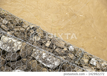 Closeup of muddy floodwater rushing through a swollen river after heavy rainfall, carrying sediment and debris during a powerful tropical storm and extreme weather. 142992272