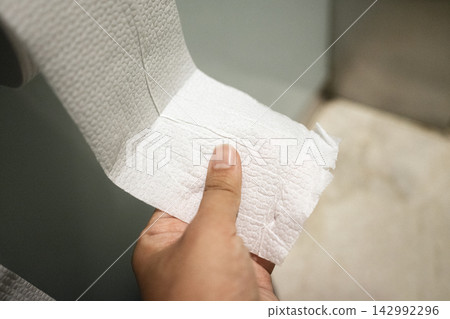 Close-up of a hand pulling a tissue paper from a roll Close-up of a hand pulling a tissue paper from a roll 142992296