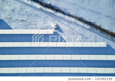 Aerial view of snow covered sustainable electric power plant with rows of solar photovoltaic panels for producing clean electrical energy. Low effectivity of renewable electricity in northern winter Aerial view of snow covered sustainable electric power plant with rows of solar photovoltaic panels for producing clean electrical energy. Low effectivity of renewable electricity in northern winter 142992299