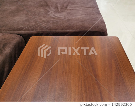 Close-up of modern wooden table top with brown sofa background. Close-up of modern wooden table top with brown sofa background. 142992300