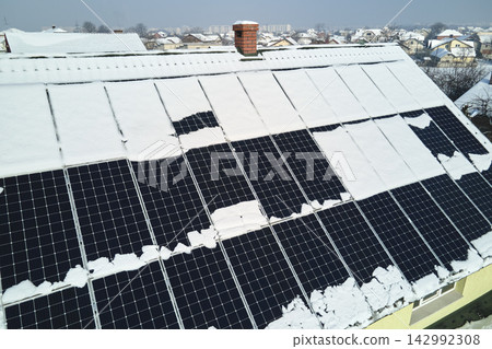 Aerial view of house roof with solar panels covered with snow melting down in winter end for producing clean energy. Concept of low effectivity of renewable electricity in northern region Aerial view of house roof with solar panels covered with snow melting down in winter end for producing clean energy. Concept of low effectivity of renewable electricity in northern region 142992308