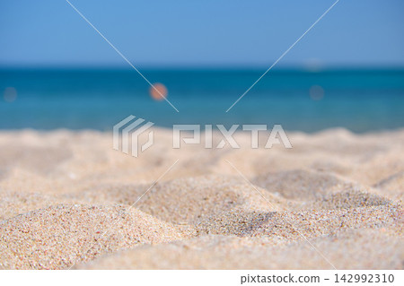 Close up of clean yellow sand surface covering seaside beach with blue sea water on background. Travel and vacations concept. Close up of clean yellow sand surface covering seaside beach with blue sea water on background. Travel and vacations concept. 142992310