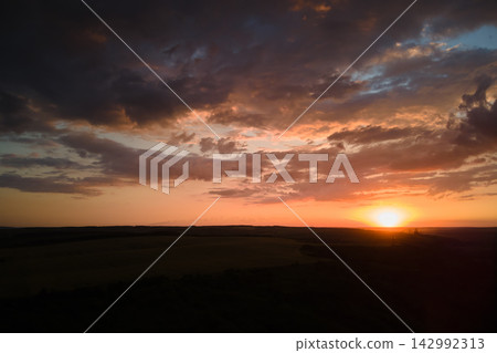 Bright colorful sunset sky with setting sun and vibrant clouds over dark landscape Bright colorful sunset sky with setting sun and vibrant clouds over dark landscape 142992313