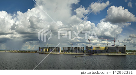Tower lifting cranes at high residential apartment buildings construction site. Real estate development on sea shore Tower lifting cranes at high residential apartment buildings construction site. Real estate development on sea shore 142992351