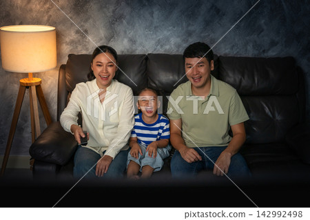 funny family (mother, father and daughter) laughing while watching comedy film on tv in the living room at night funny family (mother, father and daughter) laughing while watching comedy film on tv in the living room at night 142992498