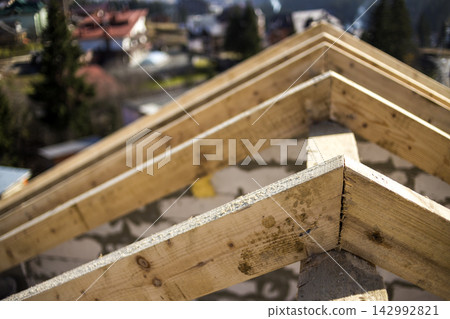 Close-up detail of roof frame of rough wooden lumber beams on background of misty mountain landscape in ecological area. Building, roofing, construction and renovation concept. Close-up detail of roof frame of rough wooden lumber beams on background of misty mountain landscape in ecological area. Building, roofing, construction and renovation concept. 142992821