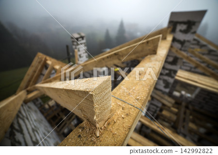 Top view of roof frame from wooden lumber beams and planks on walls made of hollow foam insulation blocks. Building, roofing, construction and renovation concept. Top view of roof frame from wooden lumber beams and planks on walls made of hollow foam insulation blocks. Building, roofing, construction and renovation concept. 142992822