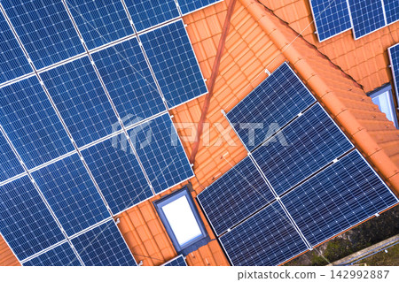 Aerial top view of new modern residential house cottage with blue shiny solar photo voltaic panels system on roof. Renewable ecological green energy production concept. Aerial top view of new modern residential house cottage with blue shiny solar photo voltaic panels system on roof. Renewable ecological green energy production concept. 142992887
