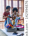 African American women packing swimwear into hardshell suitcases on bed with passports and phone 142994876