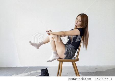 A woman stretches while sitting in a chair in a minimalist and simple studio. A woman stretches while sitting in a chair in a minimalist and simple studio. 142996604