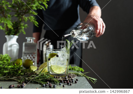 Gin is poured from the bottle into a glass with ice and a lime wedges. Gin is poured from the bottle into a glass with ice and a lime wedges. 142996867