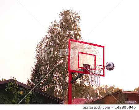 Basketball flying towards red hoop against blue sky 142996940