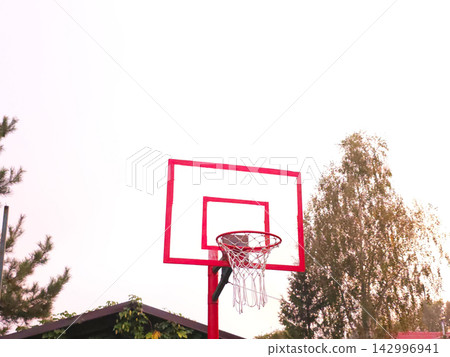 Empty red basketball hoop with net against bright sky 142996941
