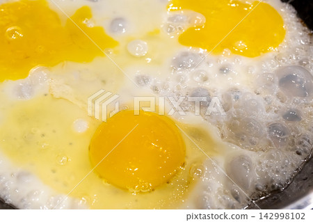 Fry eggs on pan closeup, fried cooked egg yolk and white with bubbles texture Fry eggs on pan closeup, fried cooked egg yolk and white with bubbles texture 142998102