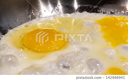 Fry eggs on pan closeup, fried cooked egg yolk and white with bubbles texture Fry eggs on pan closeup, fried cooked egg yolk and white with bubbles texture 142998941