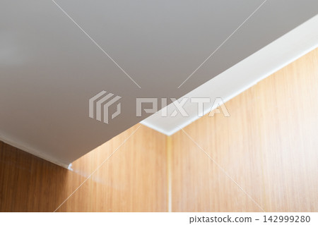 Minimal architectural close-up showing a white ceiling meeting warm wood-paneled walls Minimal architectural close-up showing a white ceiling meeting warm wood-paneled walls 142999280