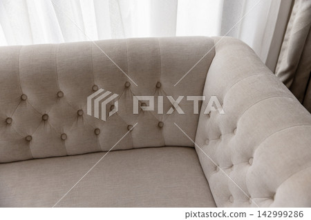 Corner of an elegant tufted beige sofa with rolled arms Corner of an elegant tufted beige sofa with rolled arms 142999286