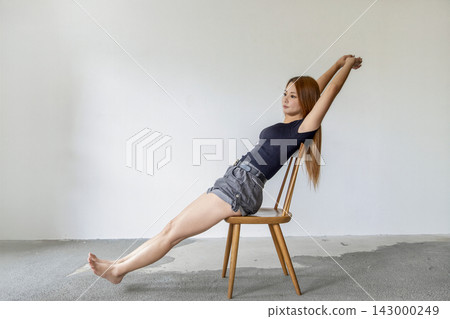 一位女士坐在簡約風格的工作室的椅子上伸展身體。 一位女士坐在簡約風格的工作室的椅子上伸展身體。 143000249