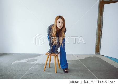 一位美麗的日本女子跪在極簡主義風格的房間裡的一張椅子上。 一位美麗的日本女子跪在極簡主義風格的房間裡的一張椅子上。 143000787
