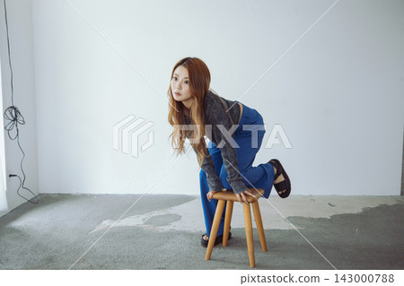 一位美麗的日本女子跪在極簡主義風格的房間裡的一張椅子上。 143000788
