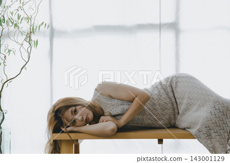 A beautiful Japanese woman relaxes and meditates on a bench by a window bathed in natural light. A beautiful Japanese woman relaxes and meditates on a bench by a window bathed in natural light. 143001129