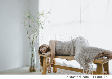 A beautiful Japanese woman relaxes and meditates on a bench by a window bathed in natural light. A beautiful Japanese woman relaxes and meditates on a bench by a window bathed in natural light. 143001130