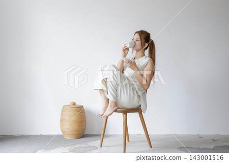 一位身著白衣的女子放鬆地坐在極簡主義的白色空間。 一位身著白衣的女子放鬆地坐在極簡主義的白色空間。 143001516