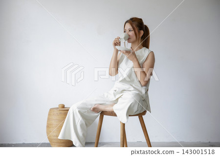 一位身著白衣的女子放鬆地坐在極簡主義的白色空間。 一位身著白衣的女子放鬆地坐在極簡主義的白色空間。 143001518