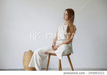 一位身著白衣的女子放鬆地坐在極簡主義的白色空間。 一位身著白衣的女子放鬆地坐在極簡主義的白色空間。 143001521