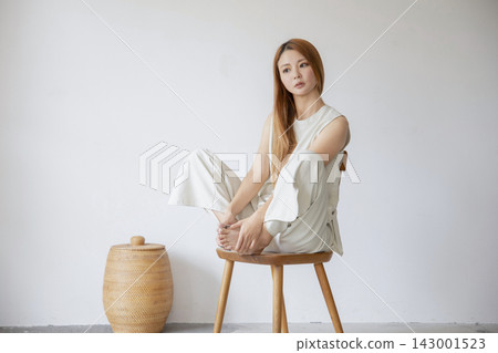 A woman dressed in white sits relaxed in a minimalist white space. A woman dressed in white sits relaxed in a minimalist white space. 143001523