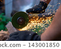 Man in protective gloves cutting metal with an angle grinder outdoors, bright sparks flying. Concept of manual labour, home workshop, DIY metalwork and work safety. 143001850