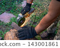 Man in protective gloves cutting metal with an angle grinder outdoors, bright sparks flying. Concept of manual labour, home workshop, DIY metalwork and work safety. 143001861