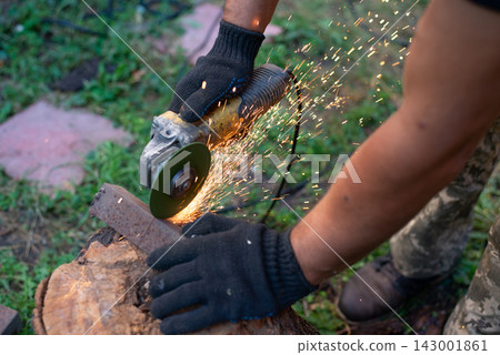 Man in protective gloves cutting metal with an angle grinder outdoors, bright sparks flying. Concept of manual labour, home workshop, DIY metalwork and work safety. Man in protective gloves cutting metal with an angle grinder outdoors, bright sparks flying. Concept of manual labour, home workshop, DIY metalwork and work safety. 143001861
