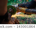 Man in protective gloves cutting metal with an angle grinder outdoors, bright sparks flying. Concept of manual labour, home workshop, DIY metalwork and work safety. 143001864