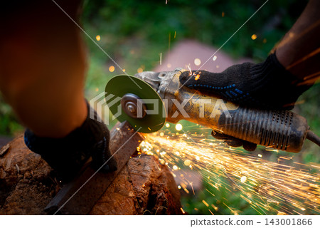 Man in protective gloves cutting metal with an angle grinder outdoors, bright sparks flying. Concept of manual labour, home workshop, DIY metalwork and work safety. Man in protective gloves cutting metal with an angle grinder outdoors, bright sparks flying. Concept of manual labour, home workshop, DIY metalwork and work safety. 143001866