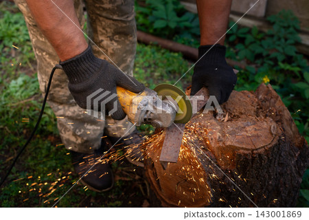 Man in protective gloves cutting metal with an angle grinder outdoors, bright sparks flying. Concept of manual labour, home workshop, DIY metalwork and work safety. Man in protective gloves cutting metal with an angle grinder outdoors, bright sparks flying. Concept of manual labour, home workshop, DIY metalwork and work safety. 143001869