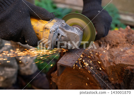 Man in protective gloves cutting metal with an angle grinder outdoors, bright sparks flying. Concept of manual labour, home workshop, DIY metalwork and work safety. 143001870
