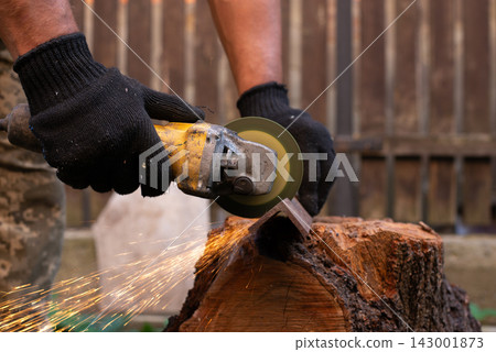 Man in protective gloves cutting metal with an angle grinder outdoors, bright sparks flying. Concept of manual labour, home workshop, DIY metalwork and work safety. Man in protective gloves cutting metal with an angle grinder outdoors, bright sparks flying. Concept of manual labour, home workshop, DIY metalwork and work safety. 143001873
