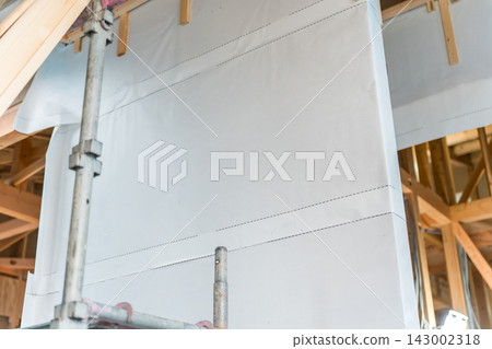 A construction site for a wooden house. A breathable waterproof membrane is being installed during the construction of a new single-family home. A construction site for a wooden house. A breathable waterproof membrane is being installed during the construction of a new single-family home. 143002318