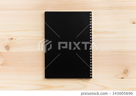 Top view of vertical black spiral notebook cover mockup on light wooden background with copy space 143005690